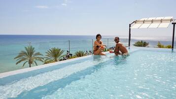 Um casal em uma piscina infinita com vista para o oceano.
