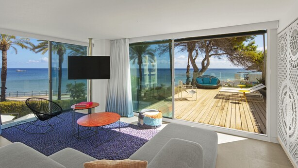 Una sala de estar moderna con un amplio ventanal que da a un balcón con vistas al mar y una terraza de madera.