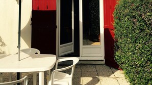 A house with a white exterior, a red door, and a sliding glass door leading to a patio area with a white table and chairs, and a large umbrella. - House of subdivision, Le Croisic  (Le Croisic)