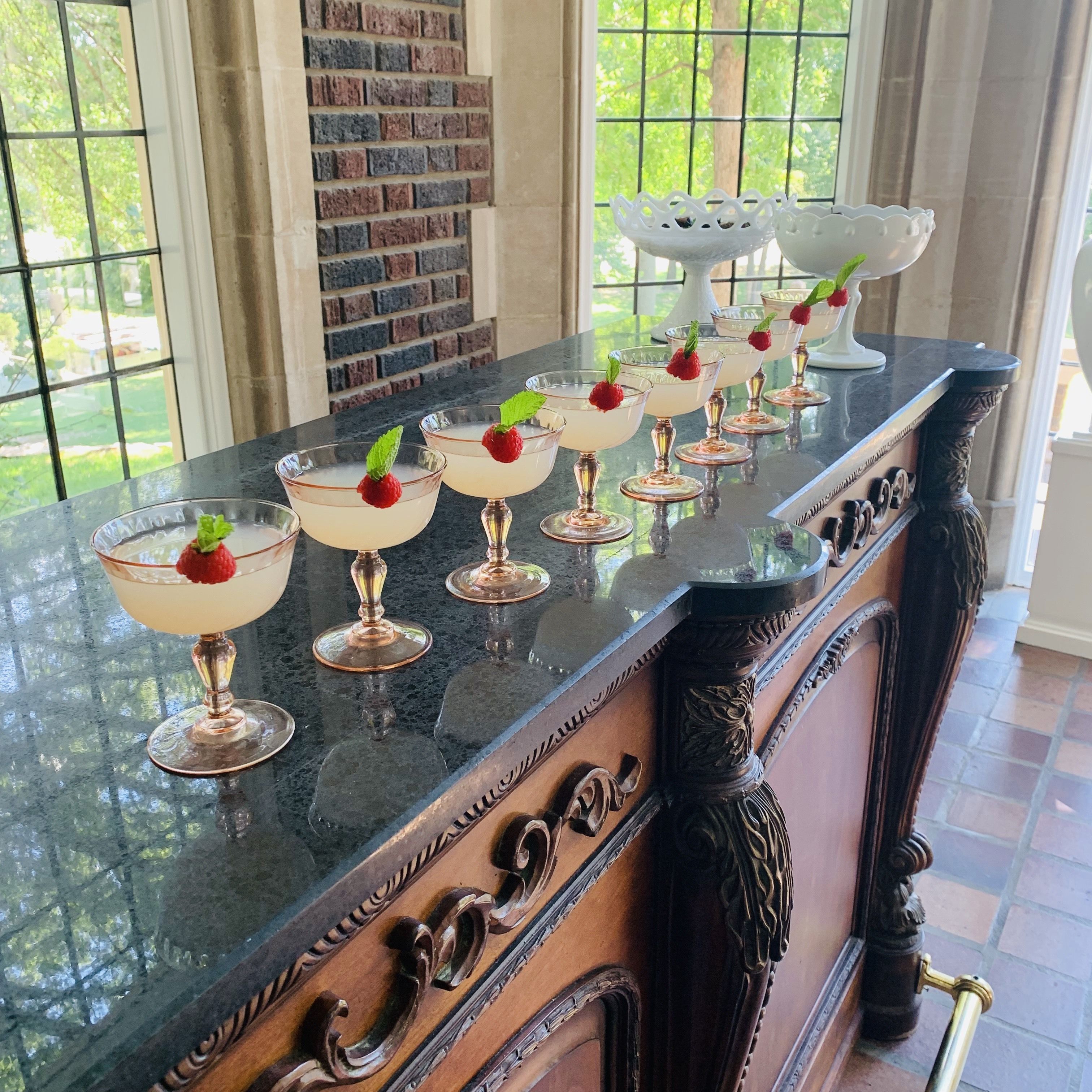 A bar area with a row of glasses on a marble countertop, each topped with a raspberry and mint leaf.