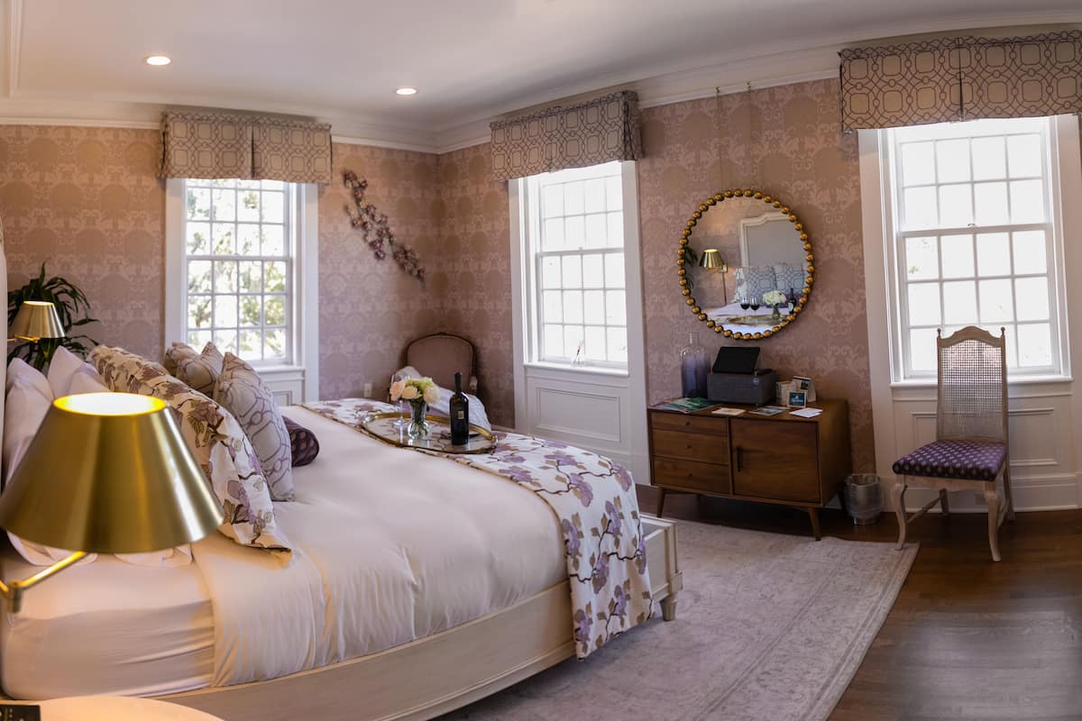 A bedroom with a bed, bedside table, dresser, chair, and a mirror.