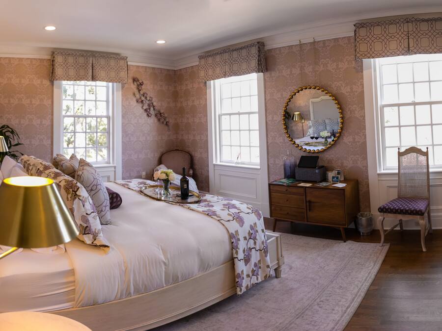 A bedroom with a bed, bedside table, dresser, chair, and a mirror.