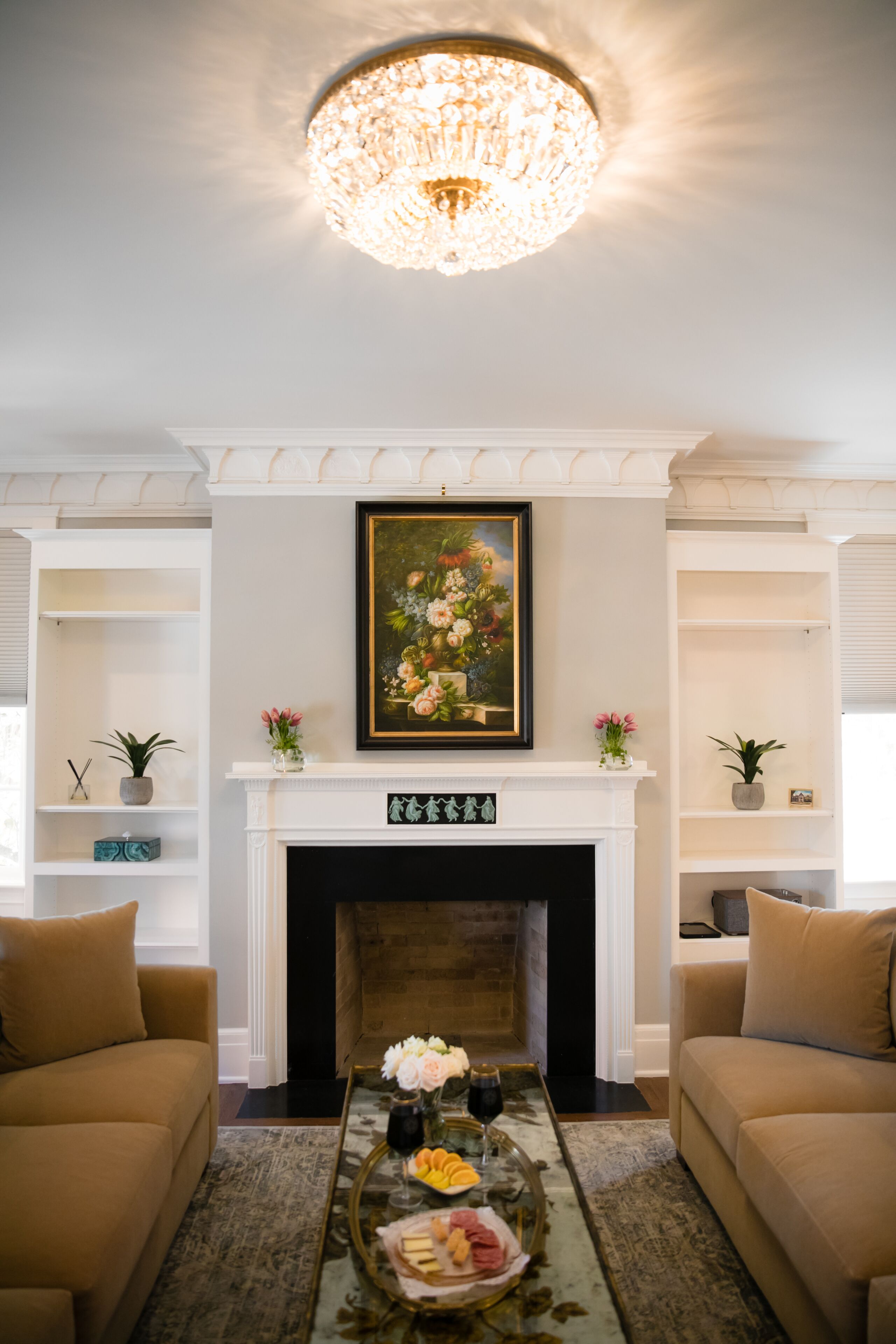 A living room with a fireplace, a chandelier, and a framed floral painting above it.