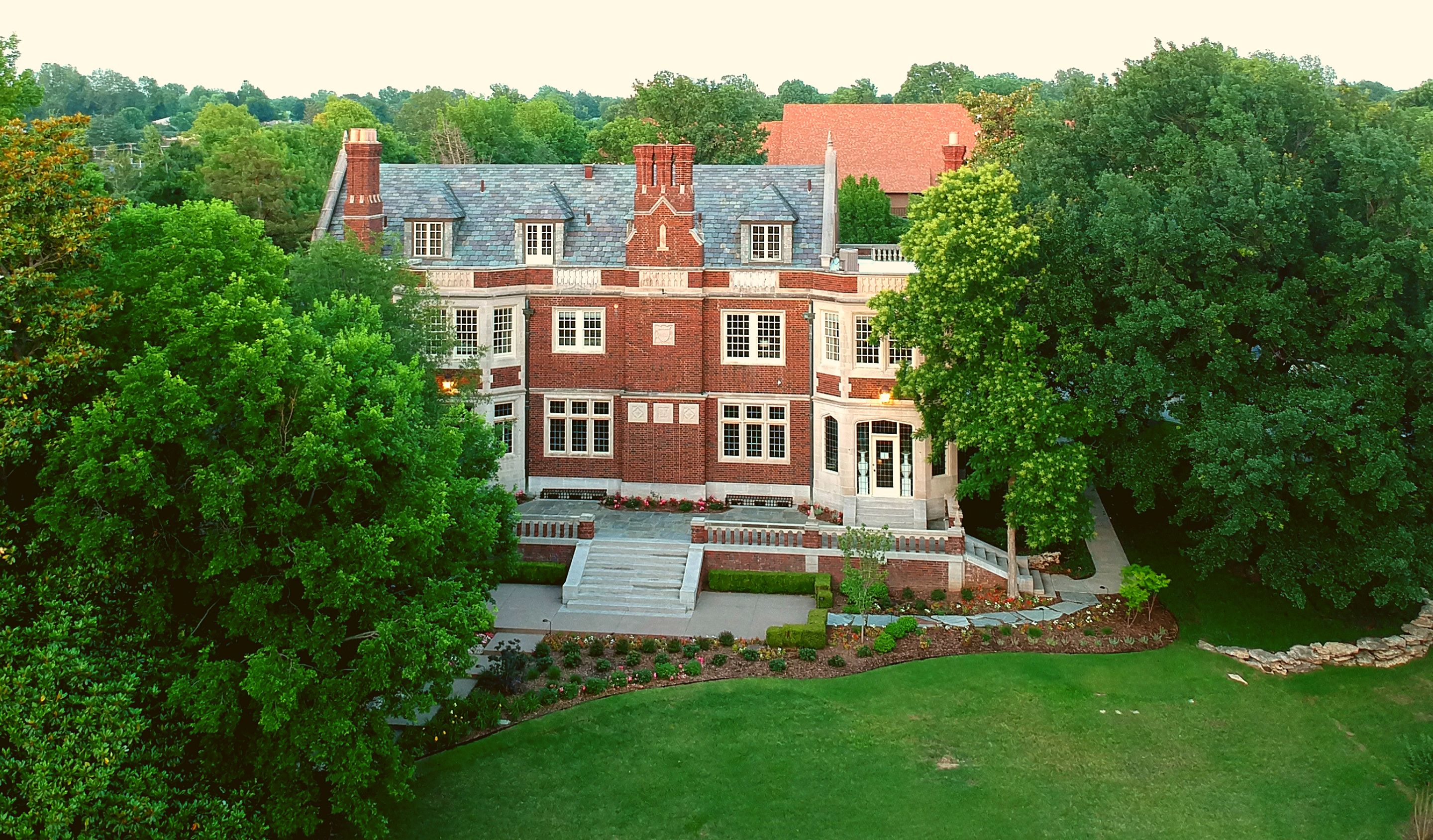 A large, multi-story brick building with a prominent entrance, surrounded by lush greenery and trees.