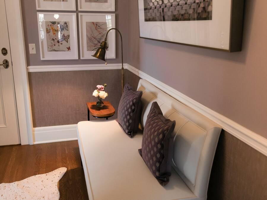 A room with a white sofa, a small side table with a lamp, and a white rug. There are four framed artworks on the wall.