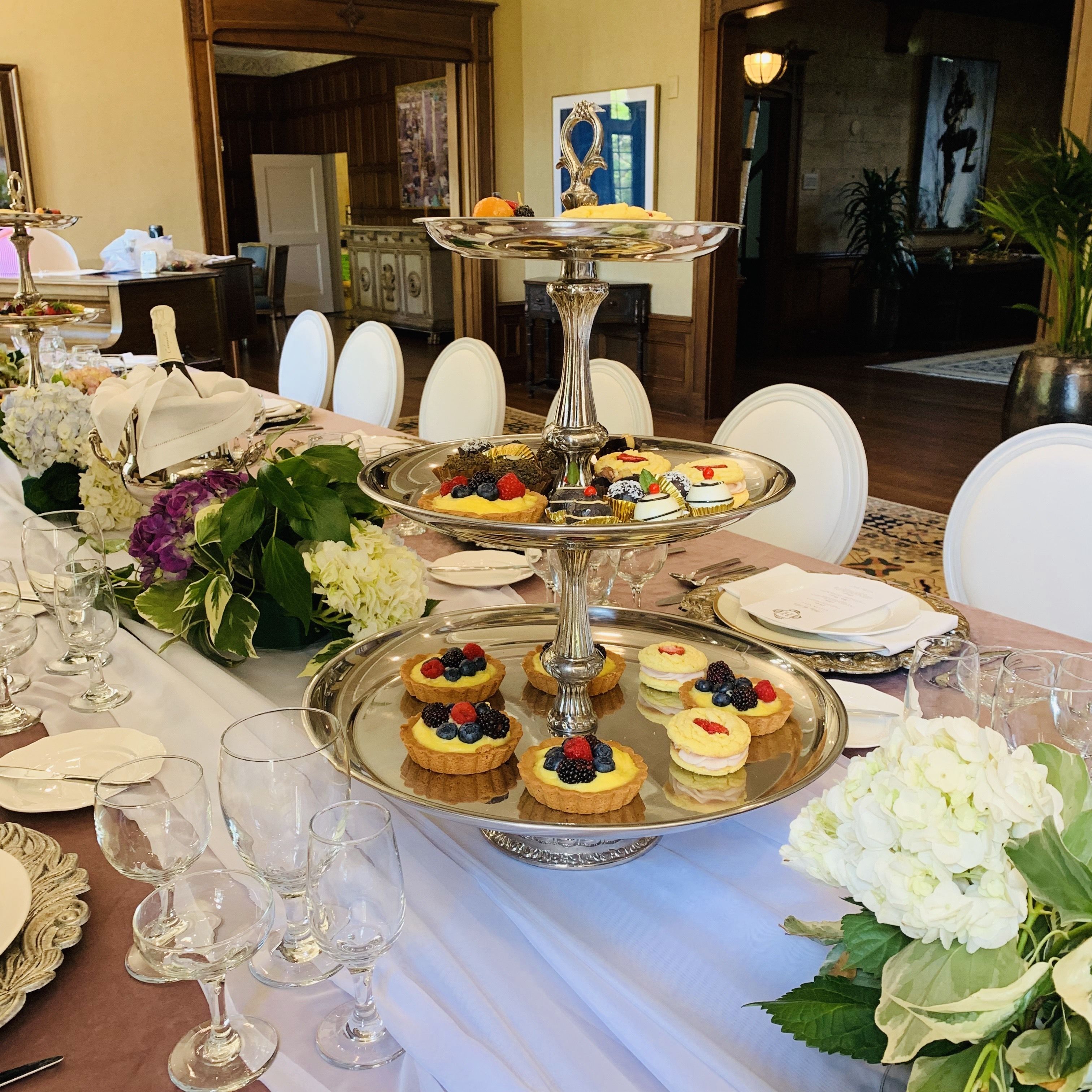 A formal dining table set with multiple tiers of dessert tarts, wine glasses, and white flowers.