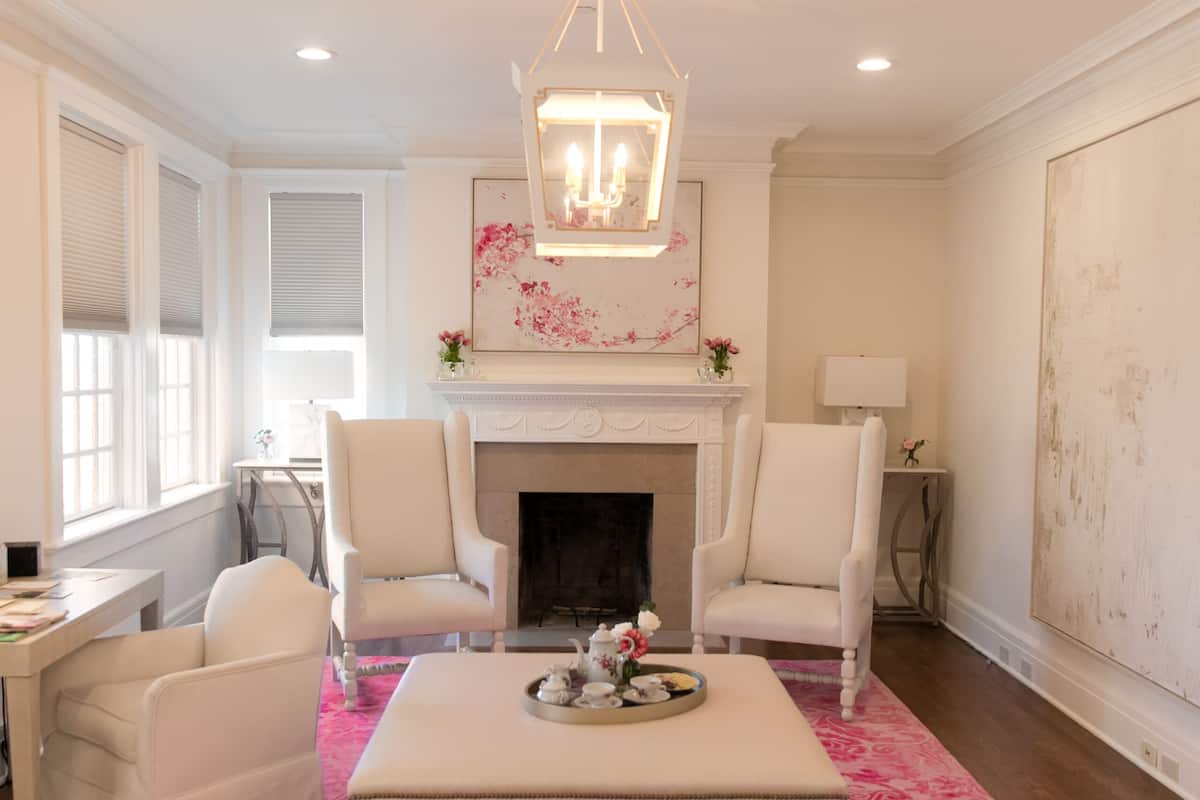 A living room with a fireplace, two white armchairs, a coffee table, and a pink patterned rug.