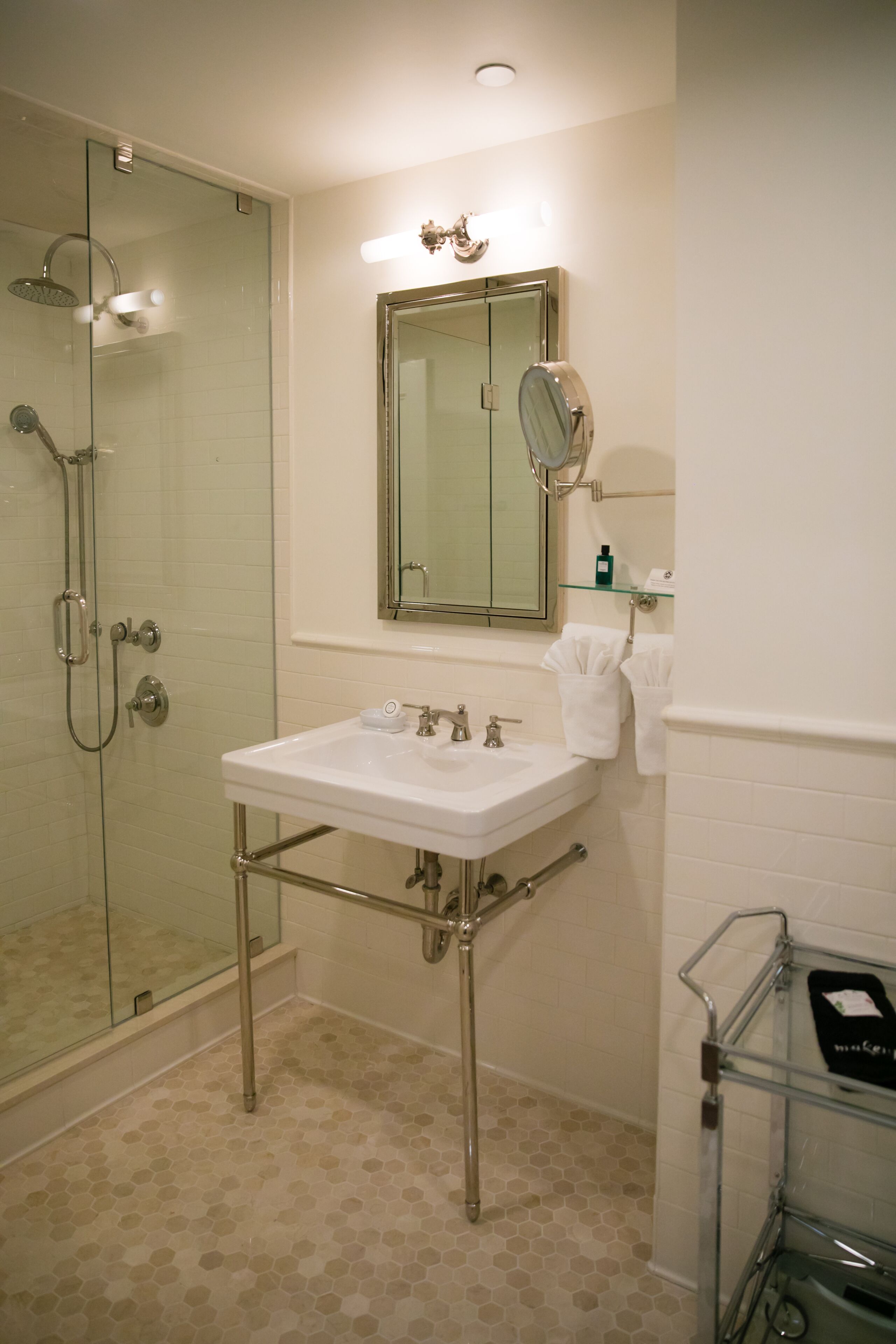 Un bagno con doccia vetrata, un lavandino bianco con accessori cromati, uno specchio sopra il lavandino e una mensola in vetro con articoli da toilette.