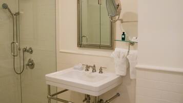 Un bagno con doccia vetrata, un lavandino bianco con accessori cromati, uno specchio sopra il lavandino e una mensola in vetro con articoli da toilette.