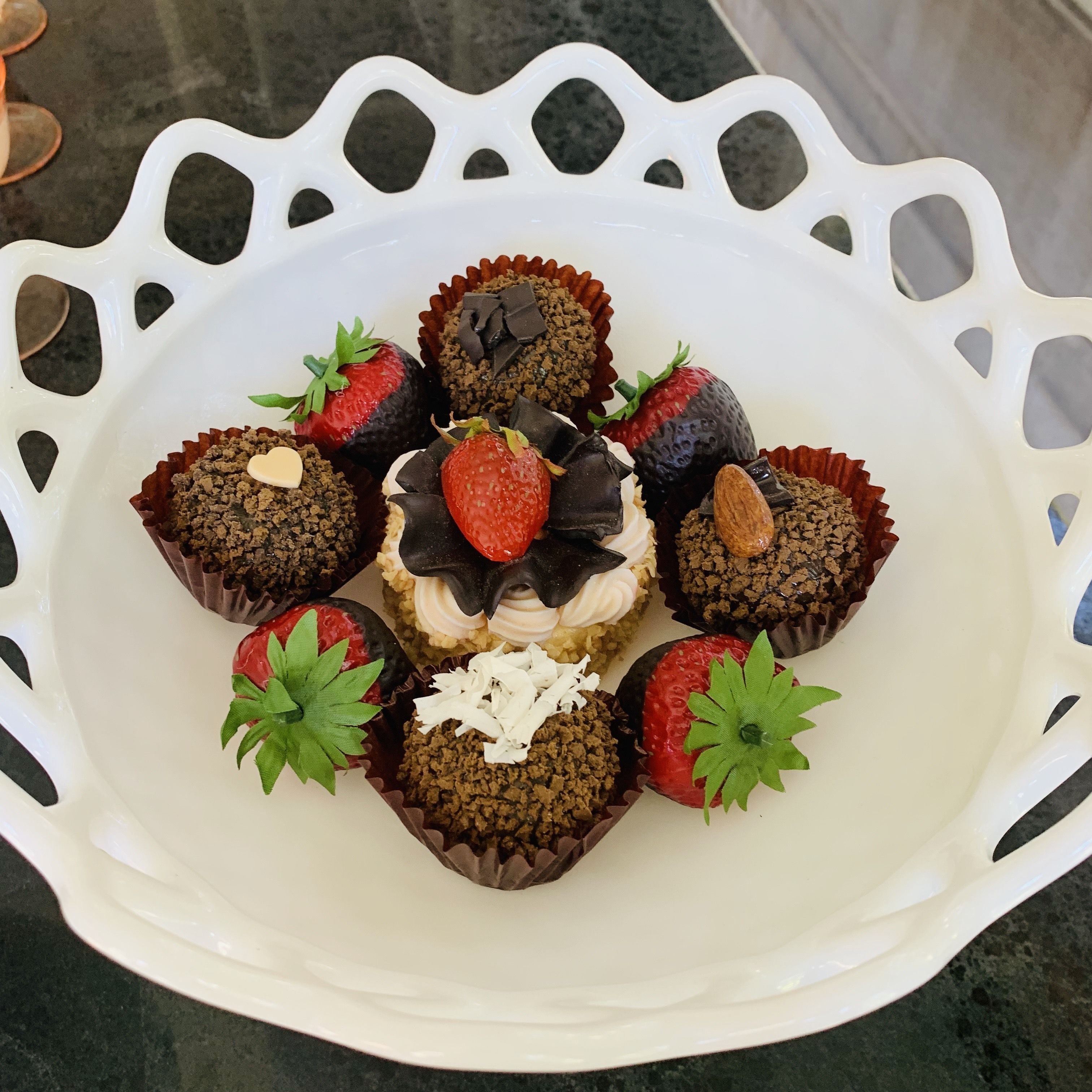 A white decorative tray with chocolate truffles and strawberries.