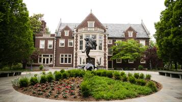 Stately building with a traditional facade and beautifully landscaped garden featuring a statue.