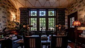 En spiseplads med et bord dækket til to personer, omgivet af stole, en potteplante og en lampe.