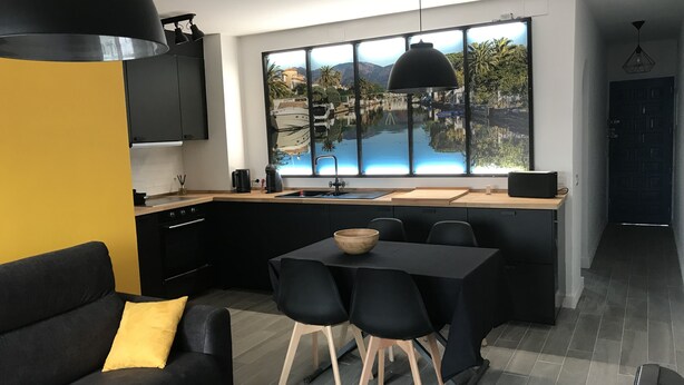 Eine moderne Küche mit einem großen Fenster, einem Essbereich mit Tisch und Stühlen sowie einem Sofa mit einem gelben Kissen.