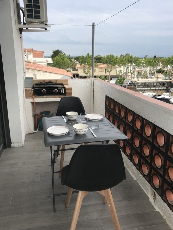 A balcony with a table set for two, a grill, and a view of the neighborhood. - Apartment very well located On mountain view canal with mooring (Empuriabrava)