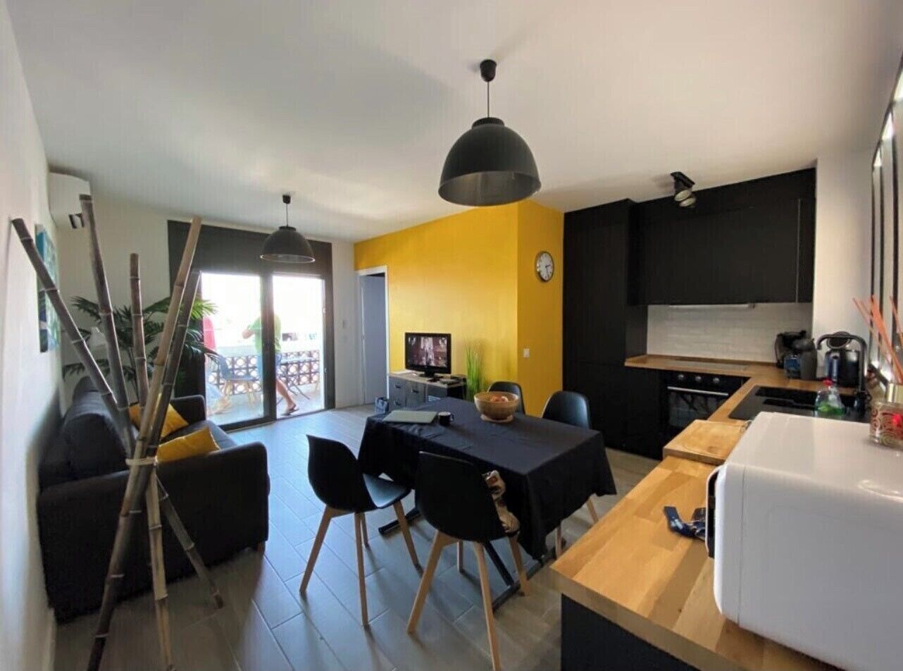 A modern kitchen with a dining area, a black sofa, and a large window.