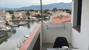 Ein Balkon mit einem Tisch für zwei Personen, Blick auf einen Yachthafen mit Booten und einer Stadtkulisse im Hintergrund.