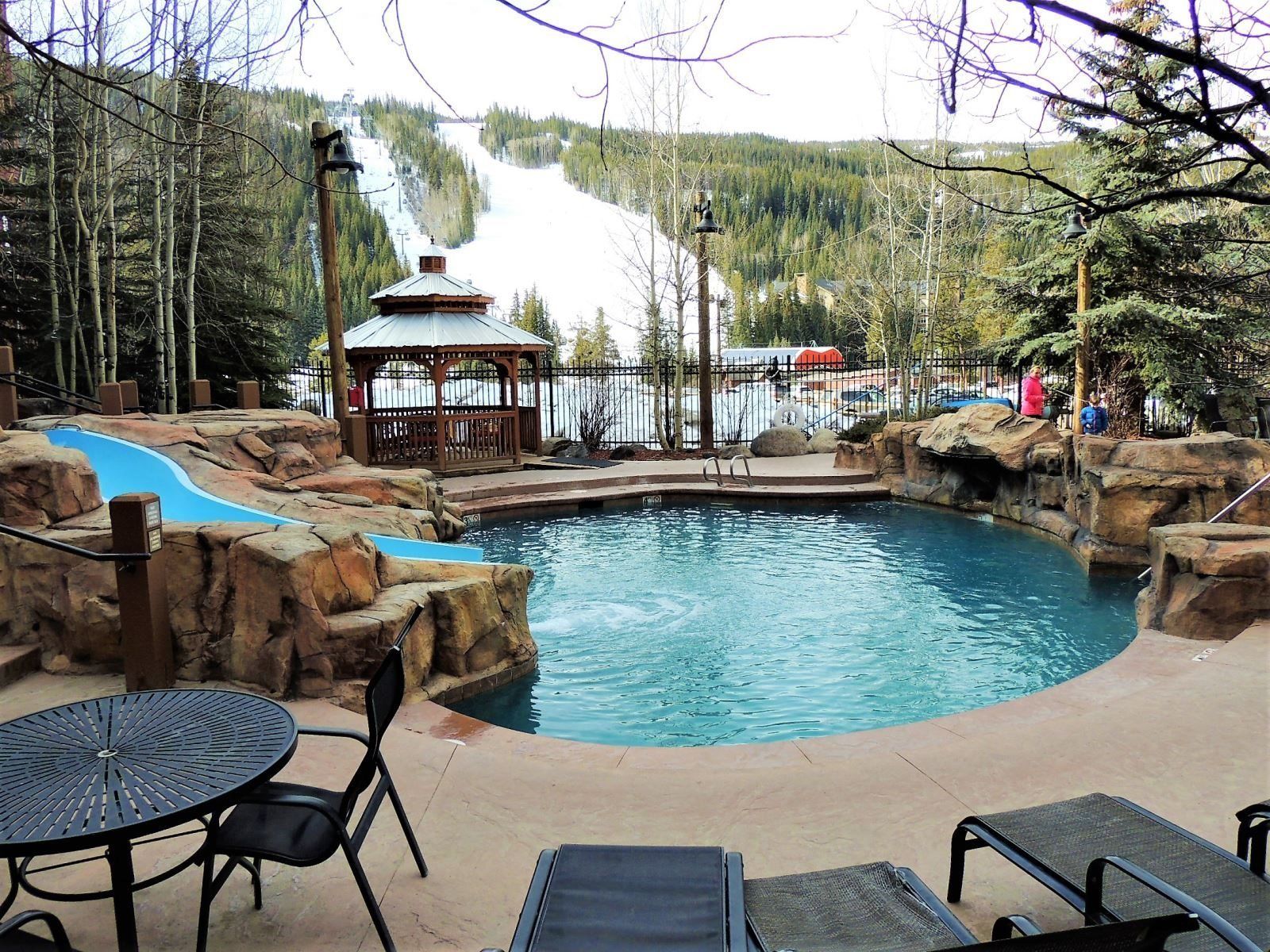 A pool area with a gazebo, seating, and a view of a snowy mountain.