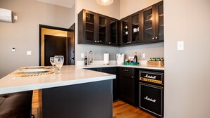 A modern kitchen with dark cabinets, a built-in dishwasher, and a countertop with a glass and a plate. - Duets Bed & Breakfast (Tulsa)