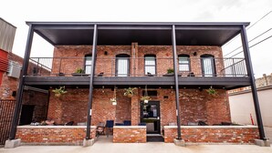 A two-story building with a brick facade, a balcony on the upper floor, and outdoor seating on the ground floor. - Duets Bed & Breakfast (Tulsa)