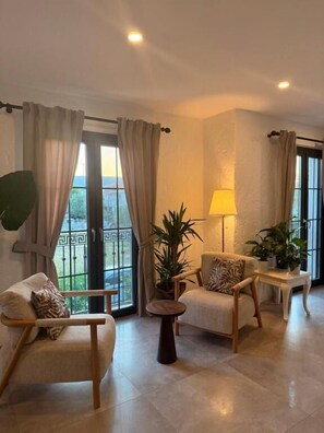 Una sala de estar con un sofá, un sillón, una mesa redonda y plantas en macetas.