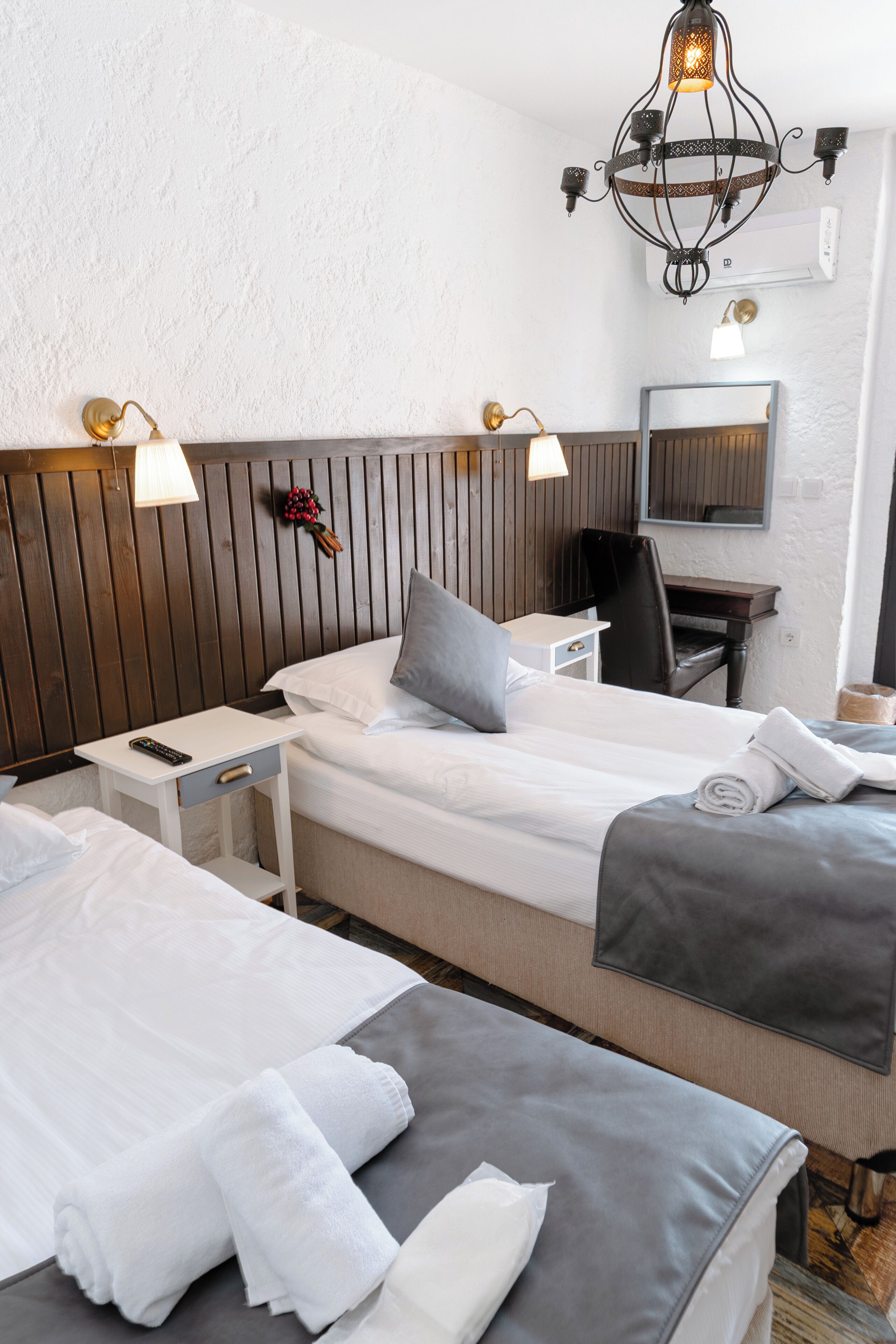 A hotel room with two beds, a desk, a chair, a mirror, and a chandelier.