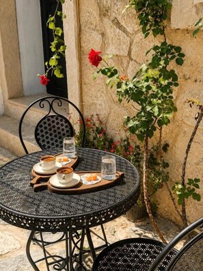 Una mesa metálica redonda con una bandeja que sostiene dos tazas y un plato de comida, frente a una pared de piedra con plantas trepadoras.