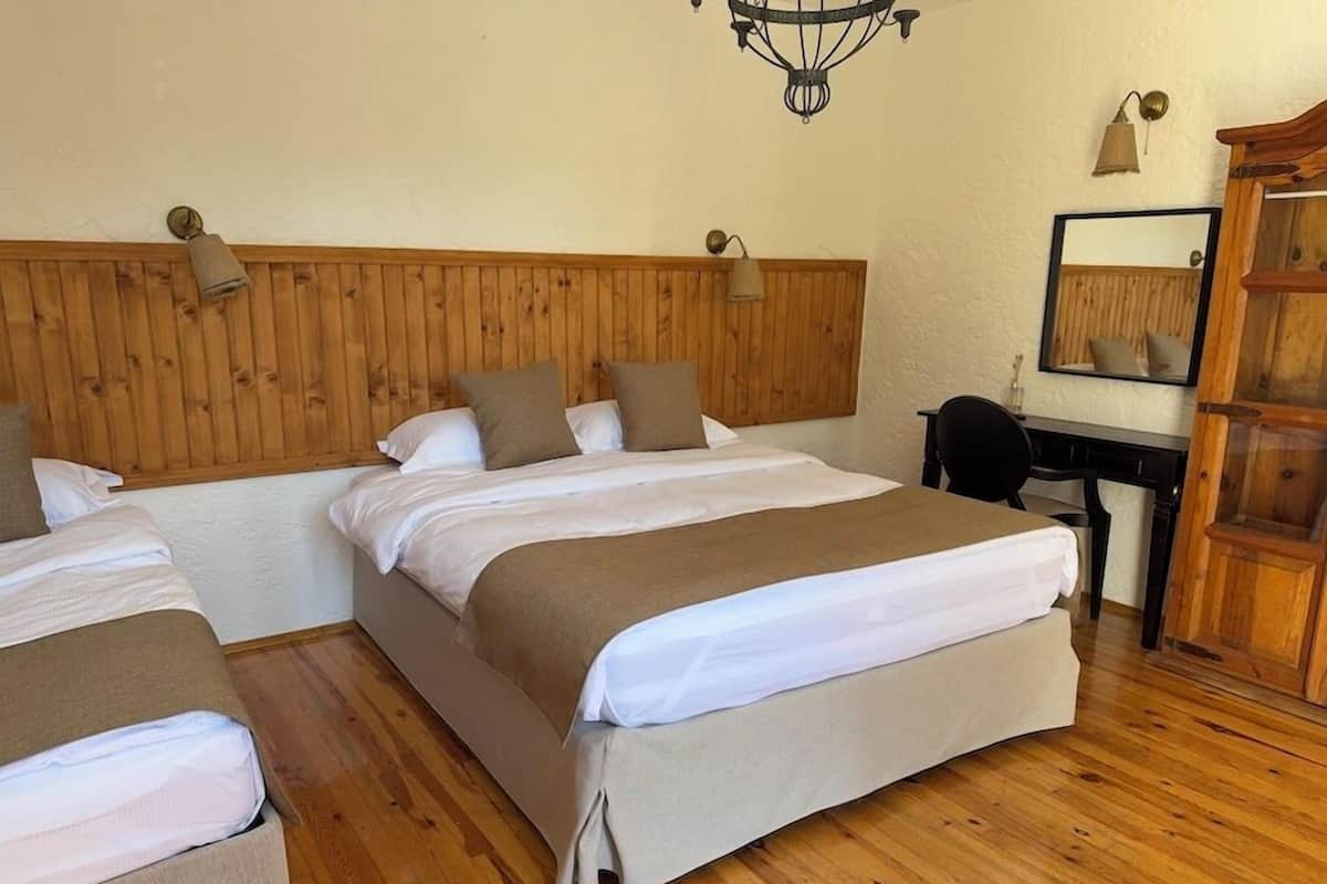 A hotel room with two beds, a wooden headboard, a desk, a mirror, and a chandelier.