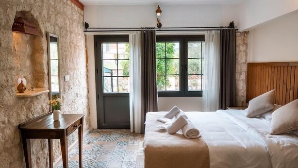 A bedroom with a bed, a nightstand, a window with curtains, and a view of the outside. - Alacati Albatross Hotel (Cesme)