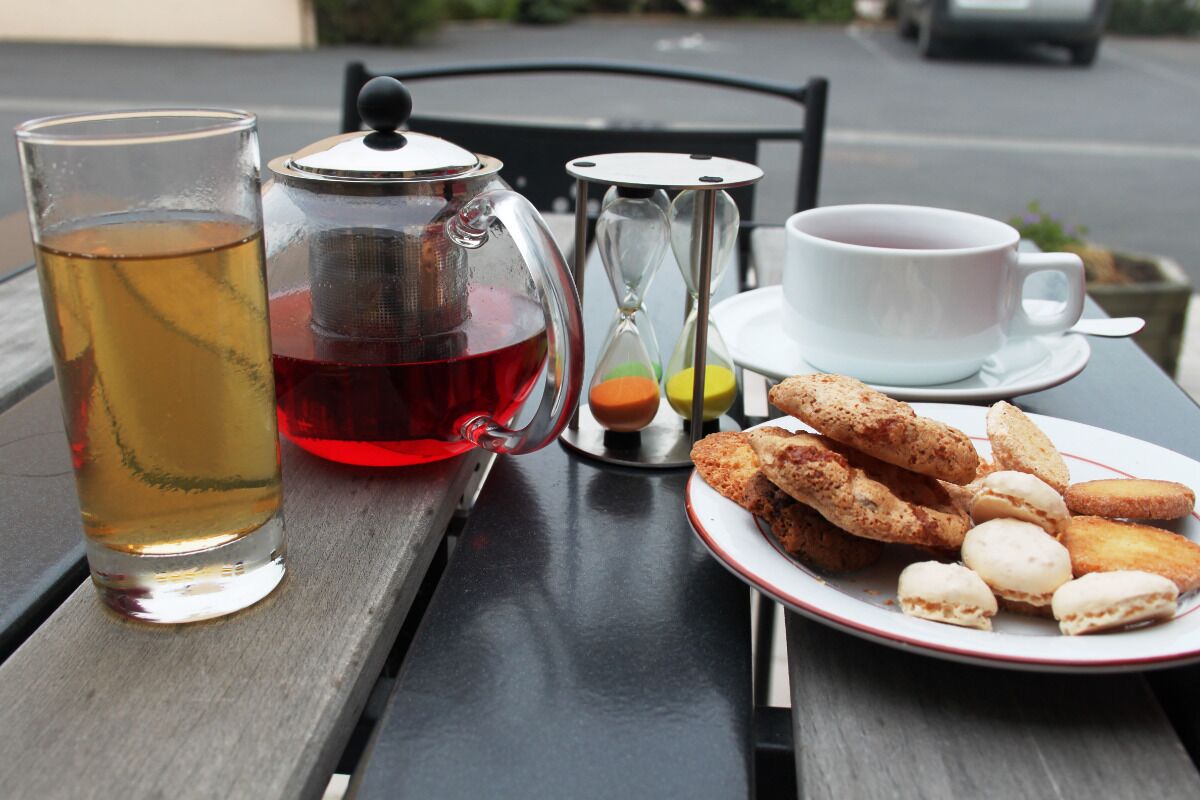 A table with a glass of tea, a teapot, an hourglass, a cup of tea, and a plate of pastries.