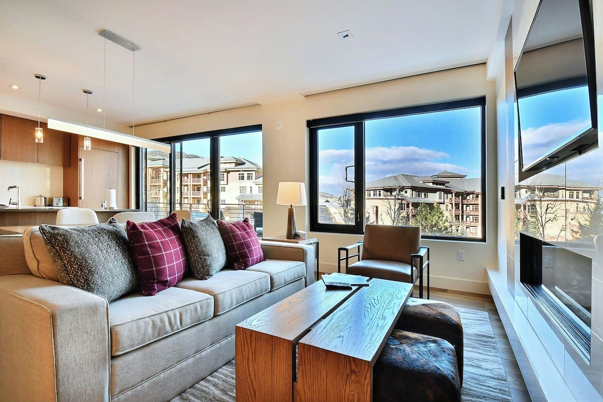 Un salón moderno con sofá, mesa de centro y ventanas amplias que ofrecen vistas de edificios.