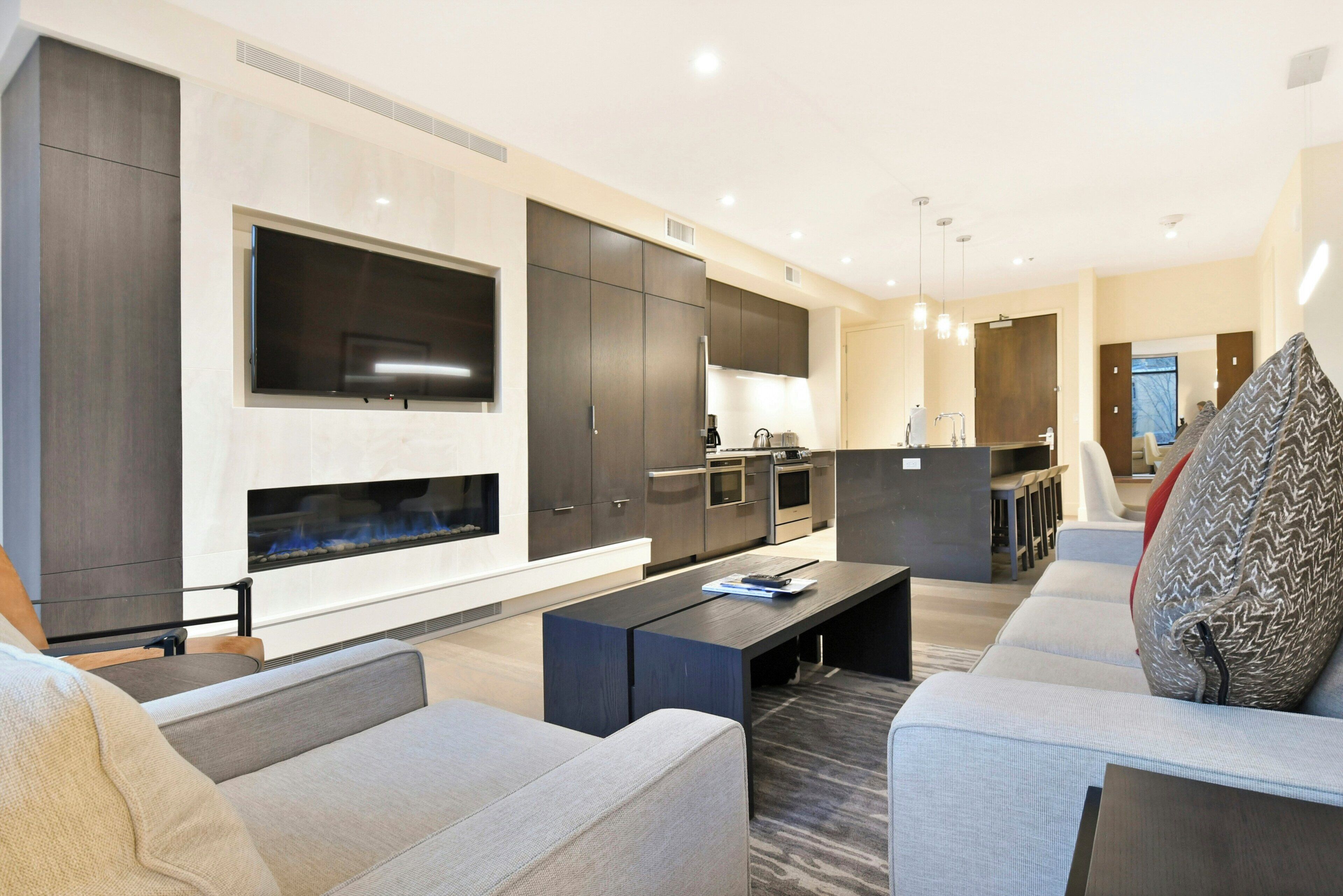 A modern living room with a fireplace, a kitchen area, and a seating area with sofas and a coffee table.