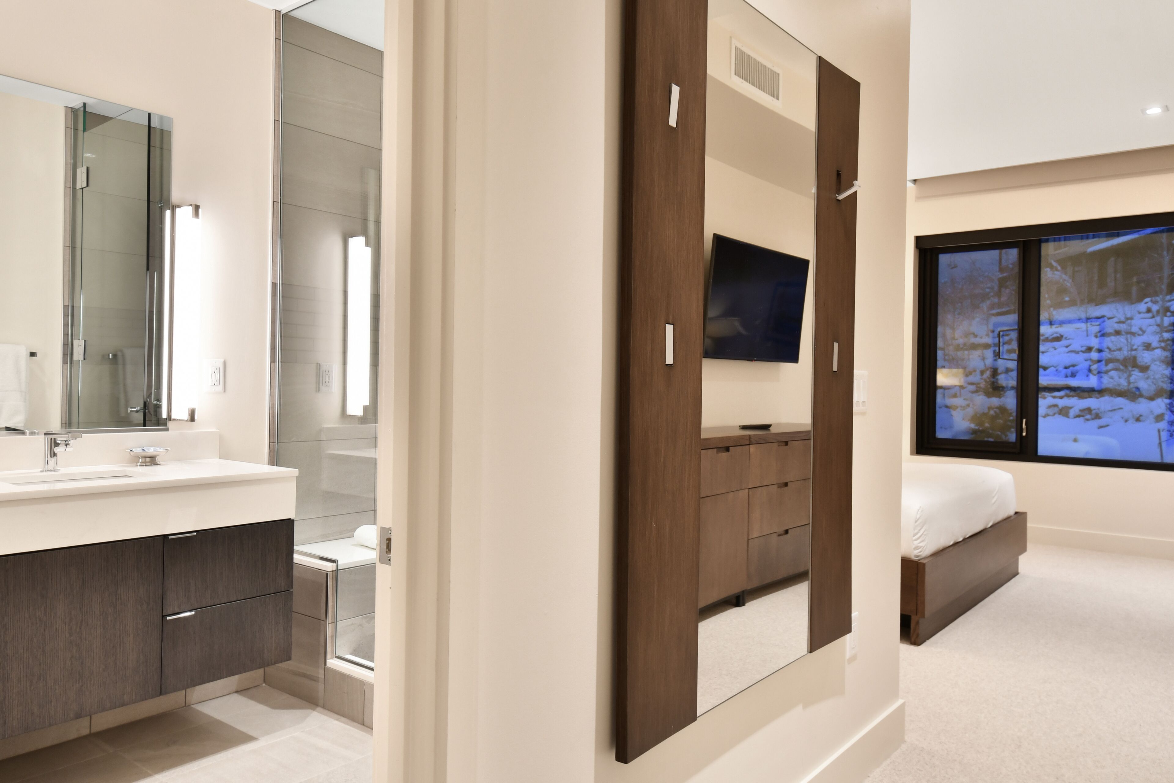Un dormitorio moderno con una cama grande, un televisor montado en la pared y una ventana con vistas a un paisaje nevado.