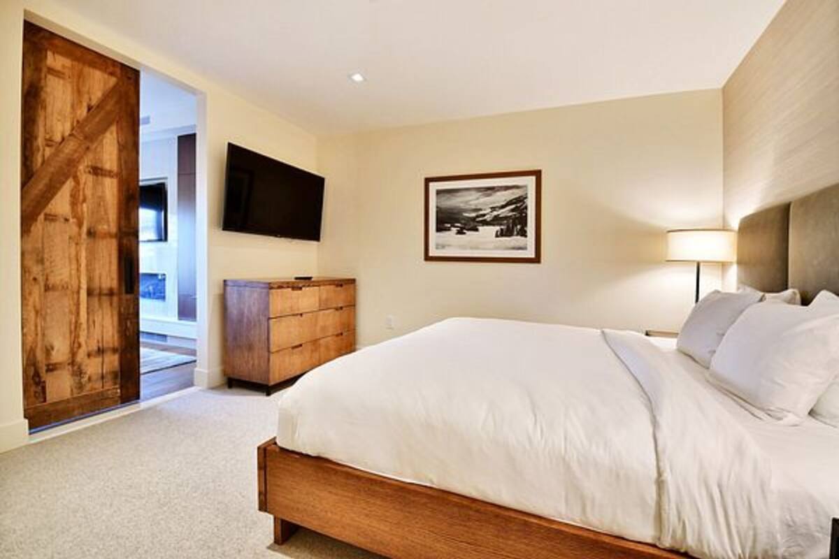 Un dormitorio con una cama de madera, un televisor montado en la pared y un cuadro enmarcado.