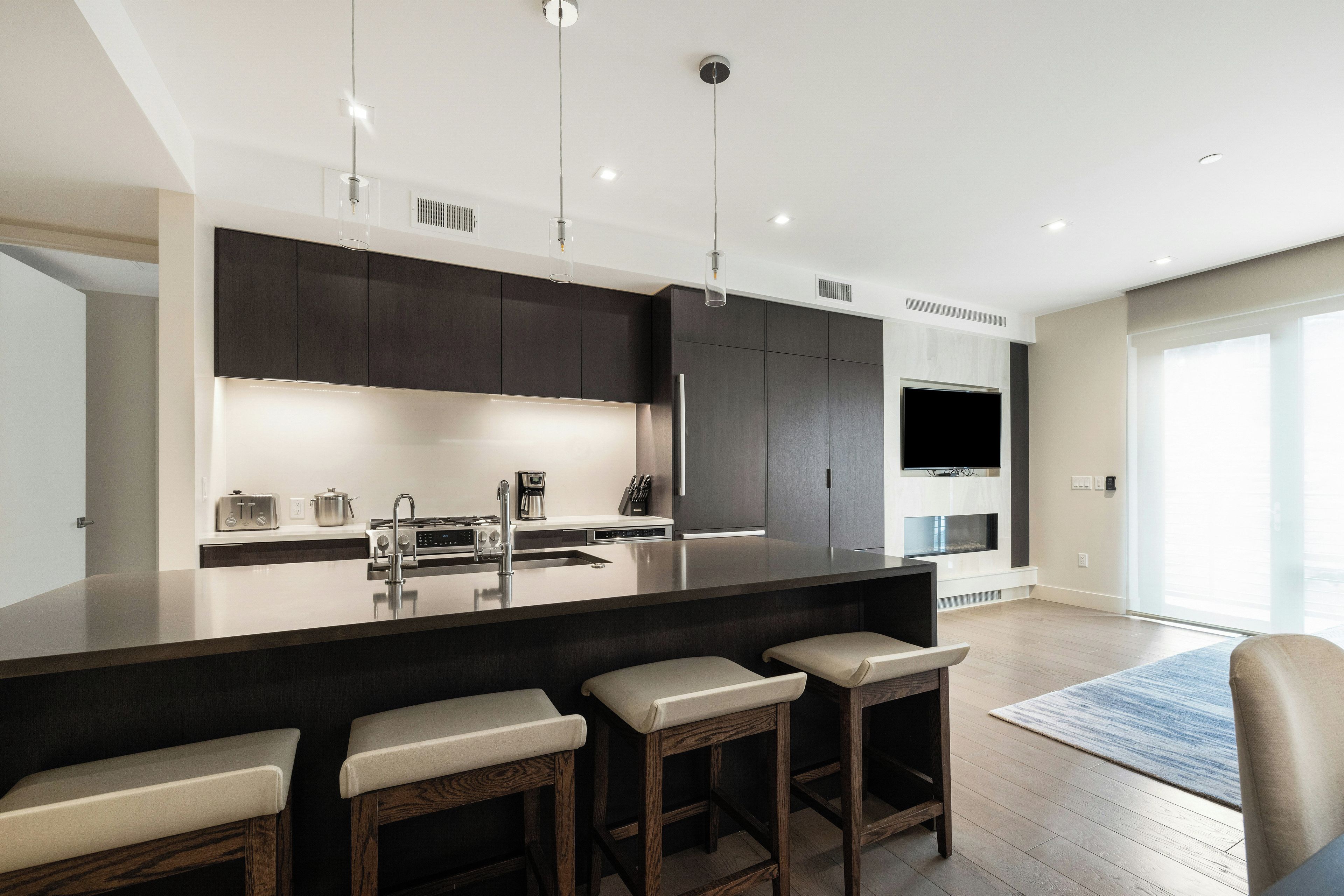 Una cocina moderna con una isla grande, taburetes de bar y un televisor de pantalla plana montado en la pared.