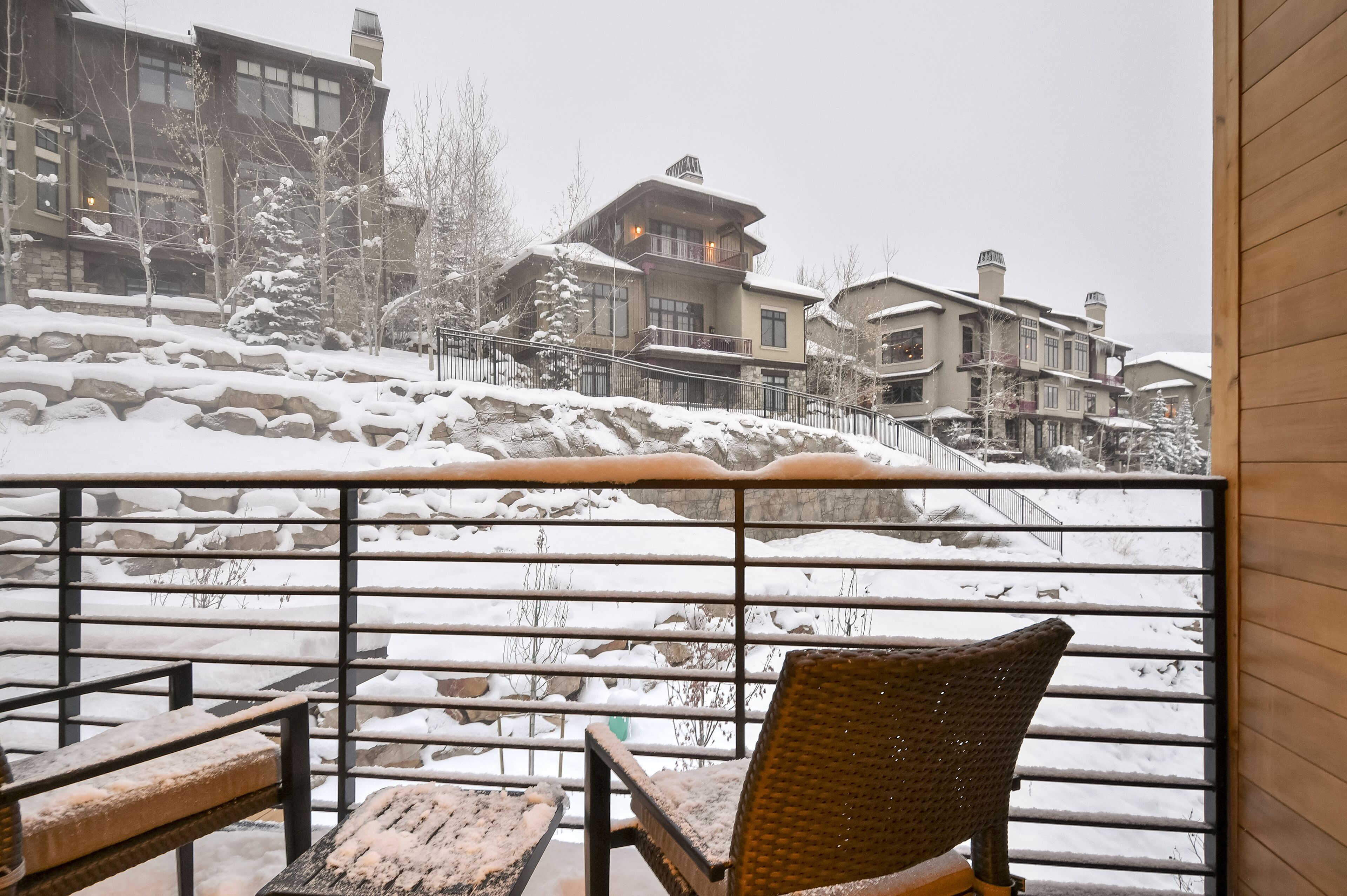A snow-covered balcony with a wicker chair and a wooden table.