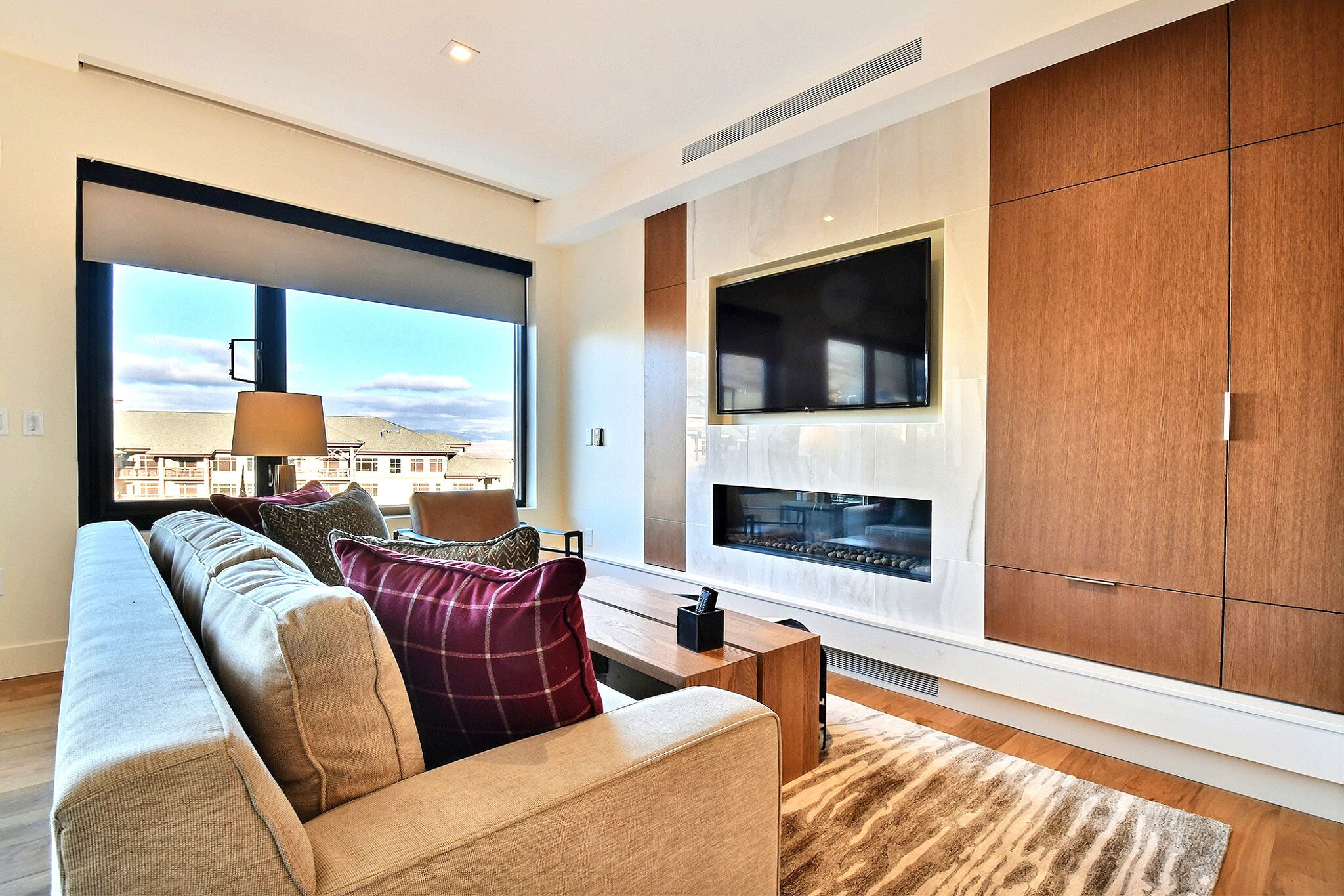 A modern living room with a large window, a sofa, a TV, and wooden cabinets.