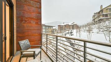 Un balcon avec une chaise, une rambarde en métal et une vue sur des bâtiments et des arbres recouverts de neige.