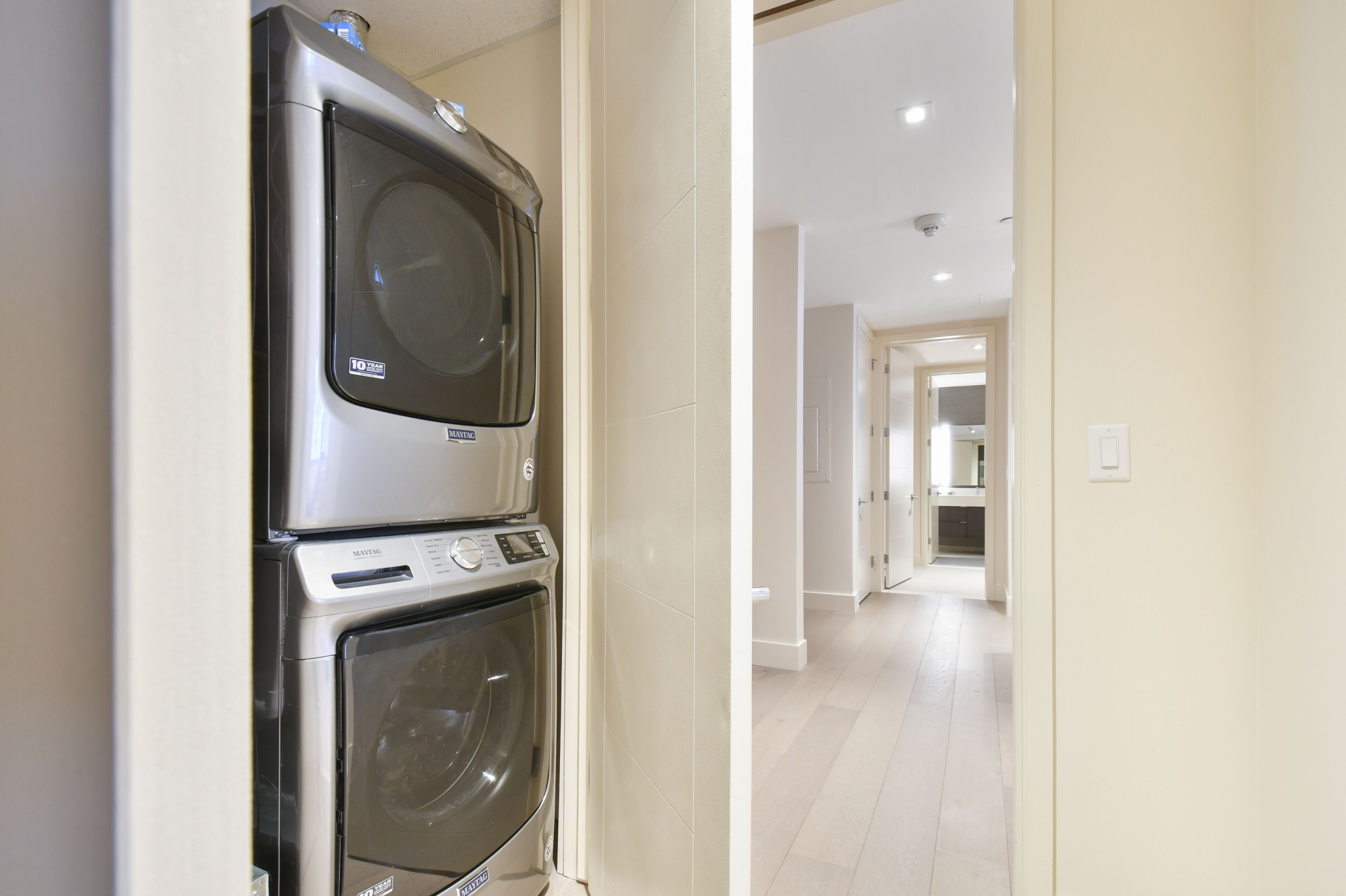 A laundry area with a front-loading washer and dryer, a hallway leading to a kitchen, and a door to another room.