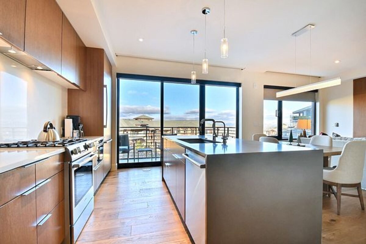 Een moderne keuken met een groot eiland, roestvrijstalen apparatuur en uitzicht op de stad.