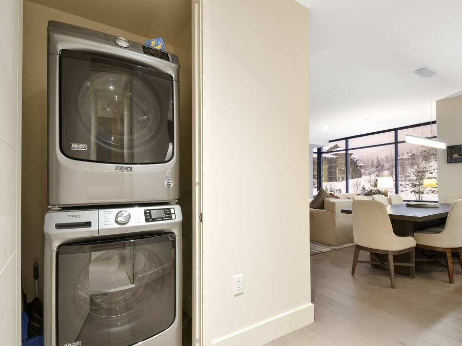 A modern kitchen with a double oven, a dining area with a table and chairs, and a view of a snowy landscape through large windows.