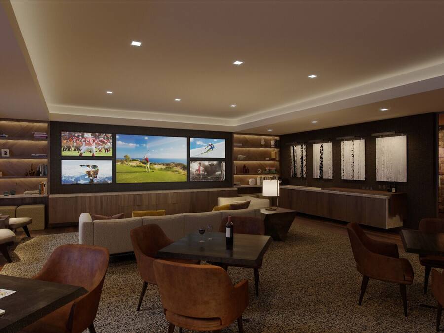 A modern lounge area with a sofa, dining table, and chairs, featuring a large TV screen displaying sports.