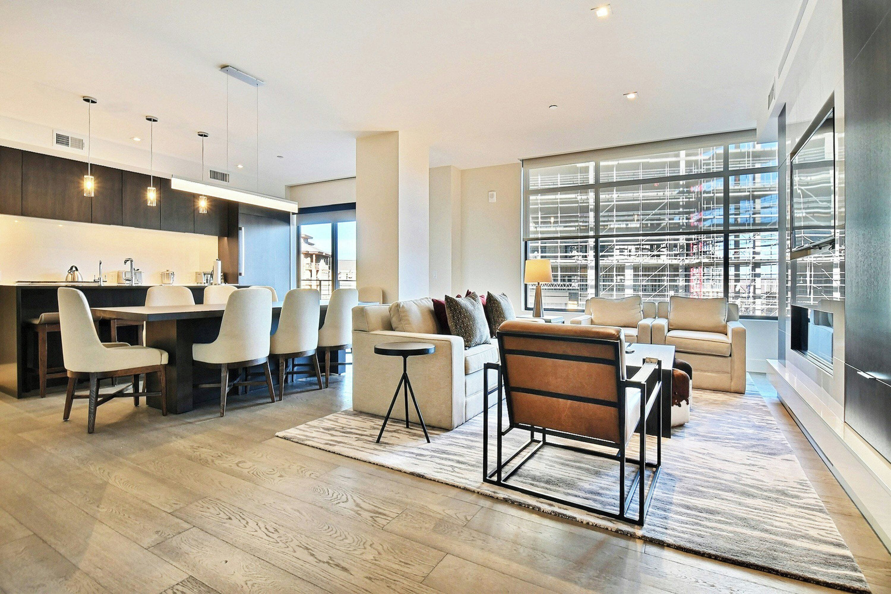 A modern living room with a dining area, large windows, and a kitchen.