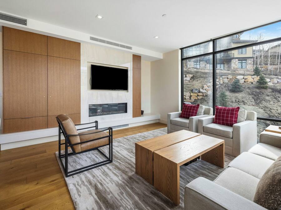 Ein modernes Wohnzimmer mit großem Fenster, einem Flachbildfernseher und einer Sitzecke mit Sofas und einem Couchtisch.