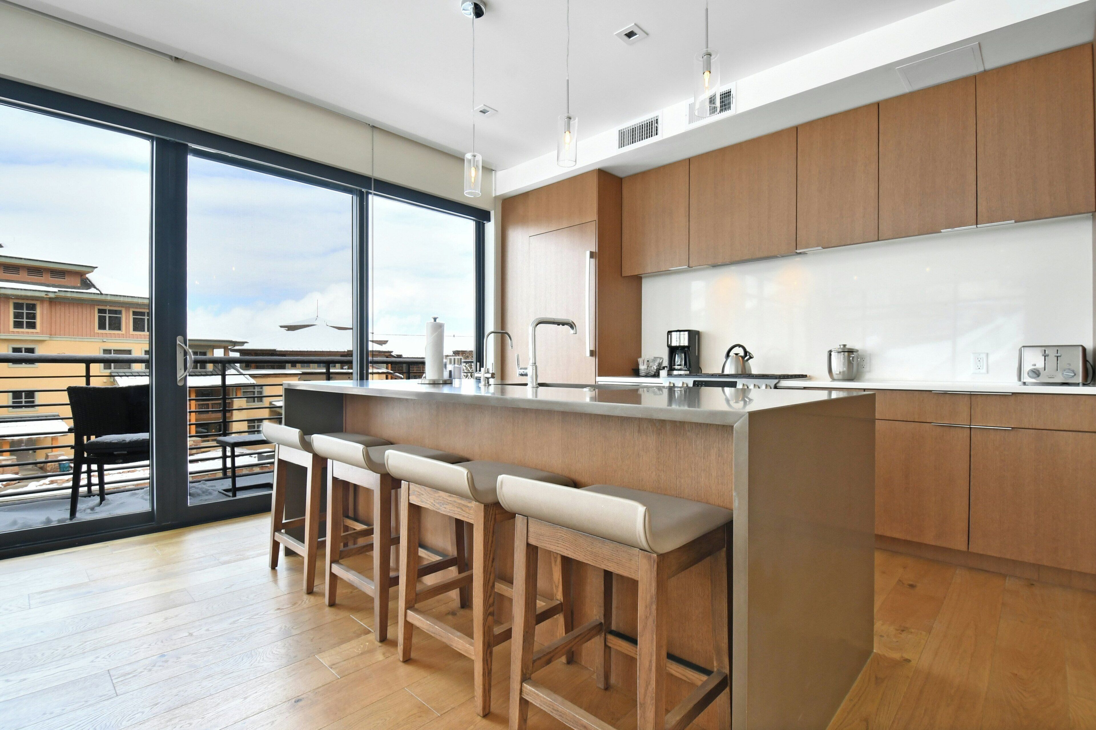 Una cocina moderna con armarios de madera, una isla grande con taburetes de bar y vistas a la ciudad a través de amplias ventanas.