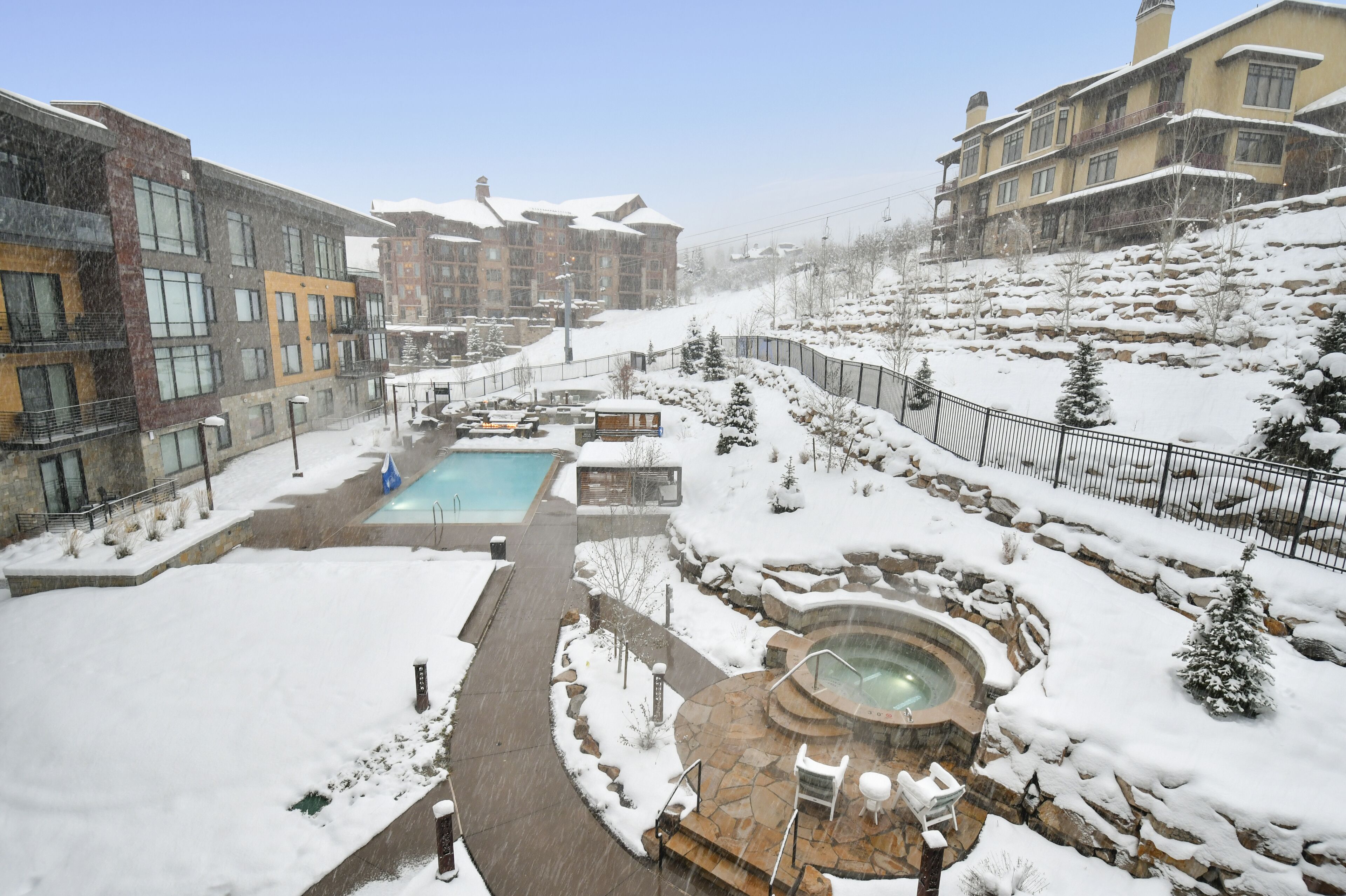 Zona exterior cubierta de nieve con piscina, bañera de hidromasaje y asientos de piedra.
