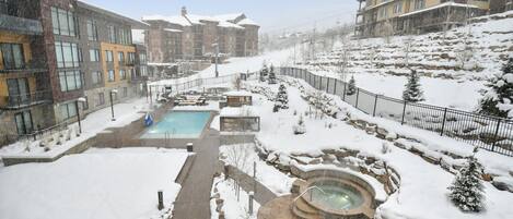 Zona exterior cubierta de nieve con piscina, bañera de hidromasaje y asientos de piedra.