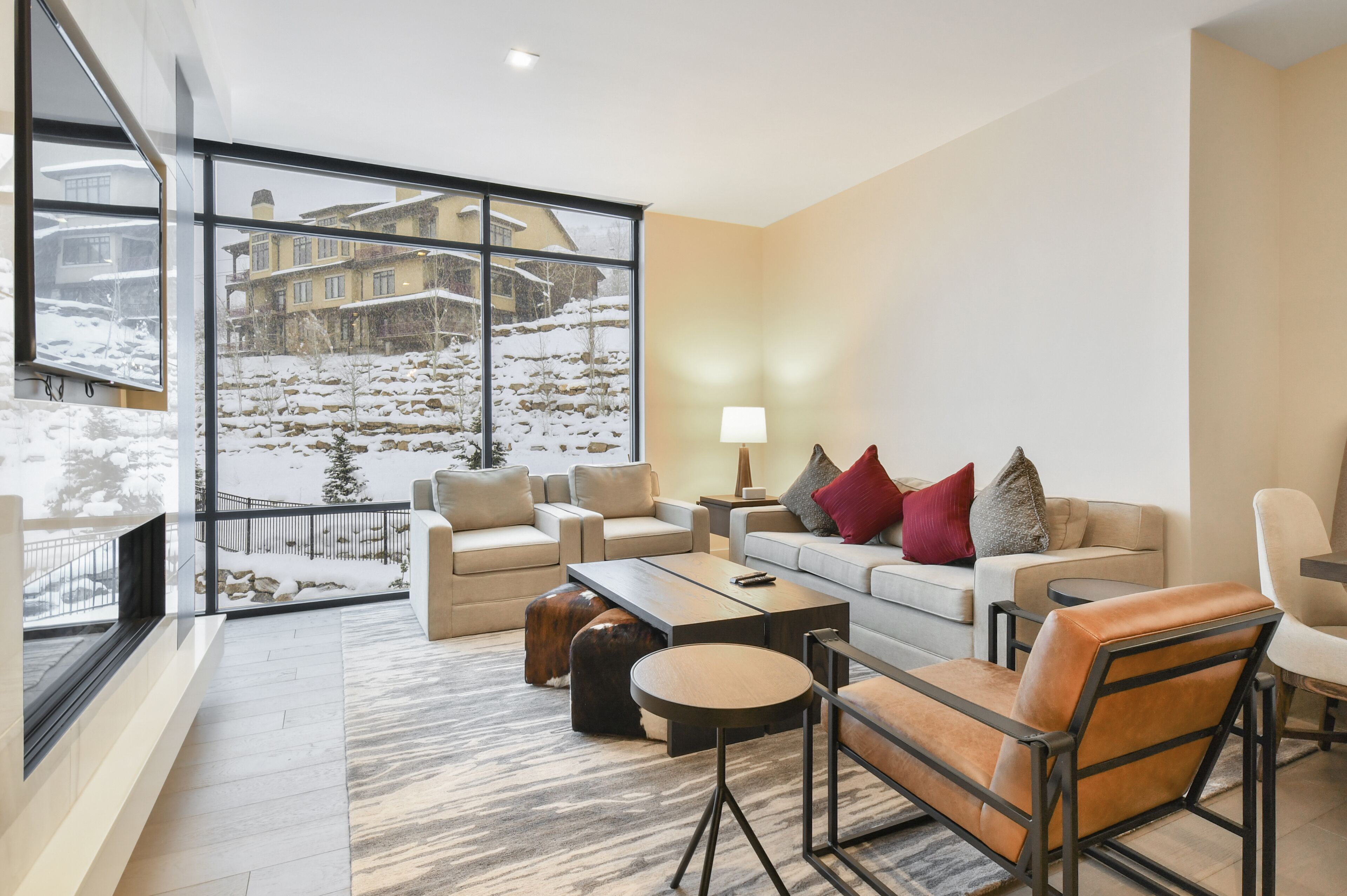 A modern living room with a large window overlooking a snowy landscape, furnished with sofas, a coffee table, and a side table.