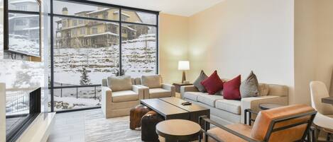 A modern living room with a large window overlooking a snowy landscape, furnished with sofas, a coffee table, and a side table.
