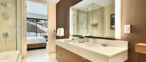 A modern bathroom with a large mirror, dual sinks, and a glass shower enclosure.