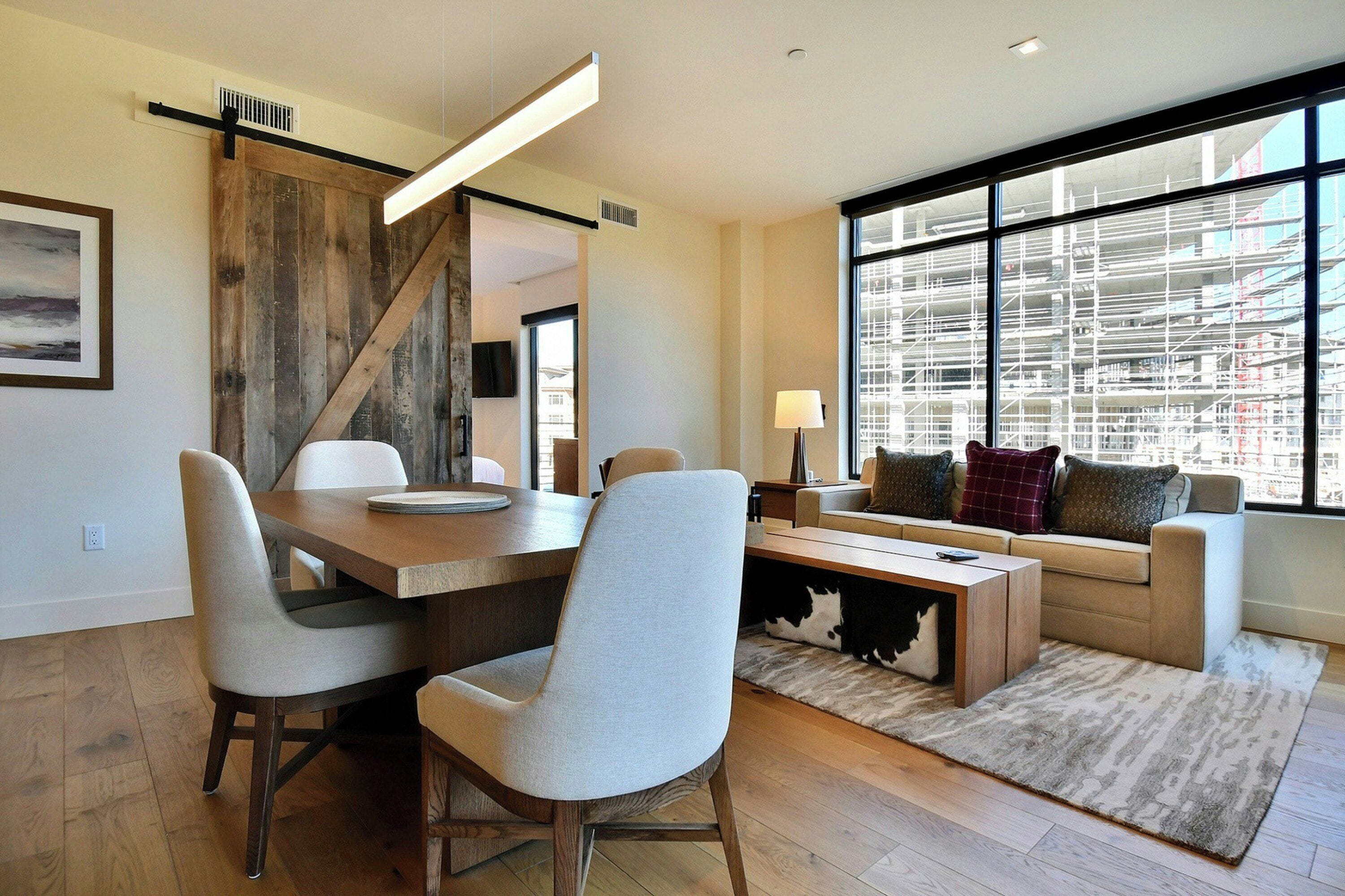 Una sala de estar moderna con comedor, ventanas amplias y vista a una obra en construcción.